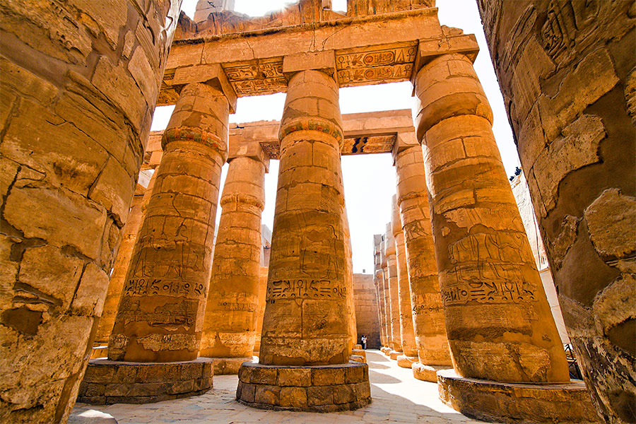 Stare podniszczone kolumny. Są ustawione w rzędach, które ciągną się wzdłuż i wszerz. Na kolumnach są hieroglify.