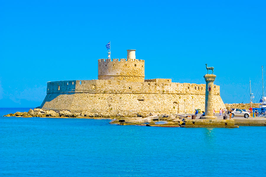 Na pierwszym planie morze. Dalej fort. Okrągły budynek z wieżą po środku. Na wieży jest flaga Grecji.